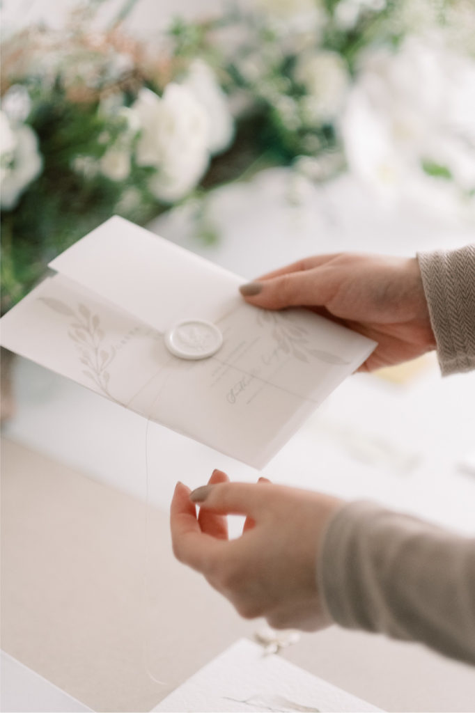 holding an wedding invitation with vellum wrap and waxseals with greenery floral